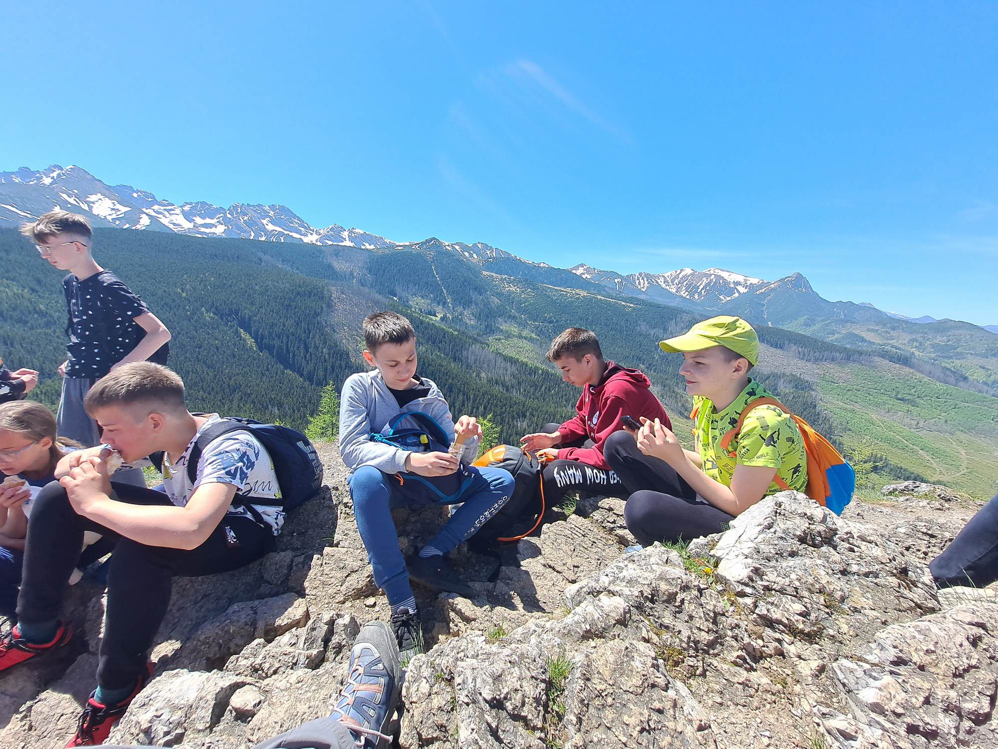 Młodzież odpoczywająca na szczycie Wielkiego Kopieńca w Tatrach Zachodnich, za nimi rozciąga się panorama gór. 