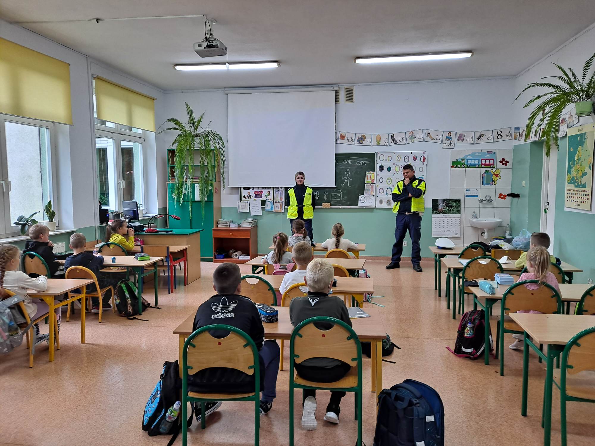 Policjanci ruchu drogowego prowadzą pogadankę z dziećmi w sali lekcyjnej