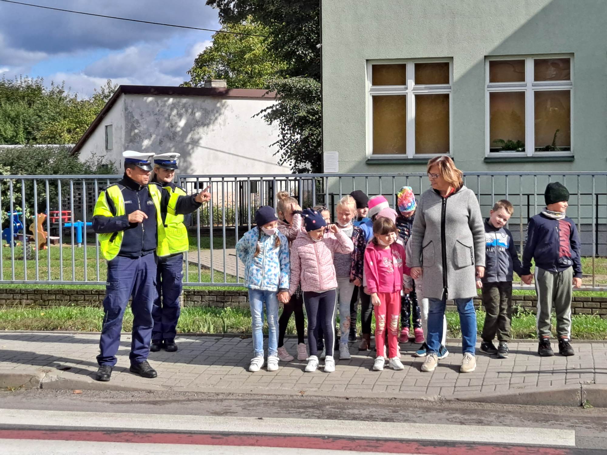 Dzieci z wychowawcą klasy pod kierunkiem policji ćwiczą przechodzenie na pasach