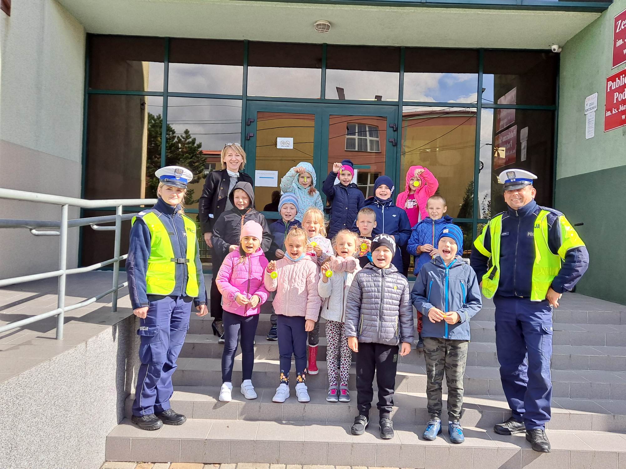 Dzieci stojące przed szkołą w towarzystwie policjantów z Wydziału Ruchu Drogowego