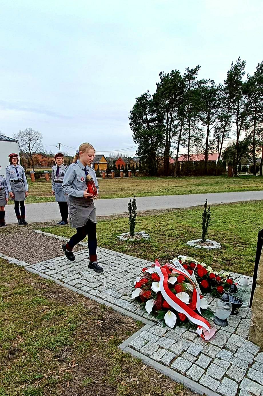 Harcerka składa znicz przy tablicy upamiętniającej Polaków ratujących Żydów pod okupacją niemiecką  w Opoce Dużej