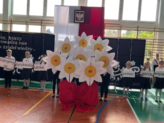 Taniec kwiatów (bukiet stokrotek) i dzieci prezentujące napisy na planszach